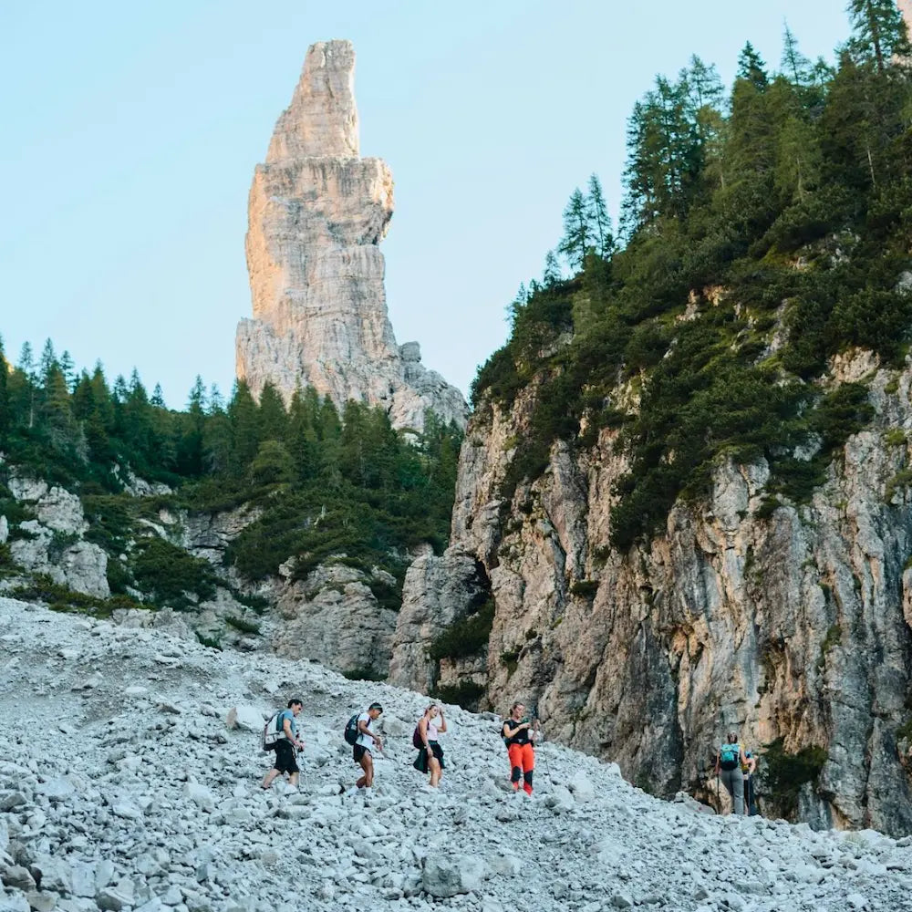 Group of hikers trekking through scree field beneath Campanile di Val Montanaia tower in Friulian Dolomites UNESCO site