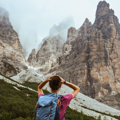 Female hiker with blue backpack admiring towering limestone cliffs in misty Friulian Dolomites Natural Park