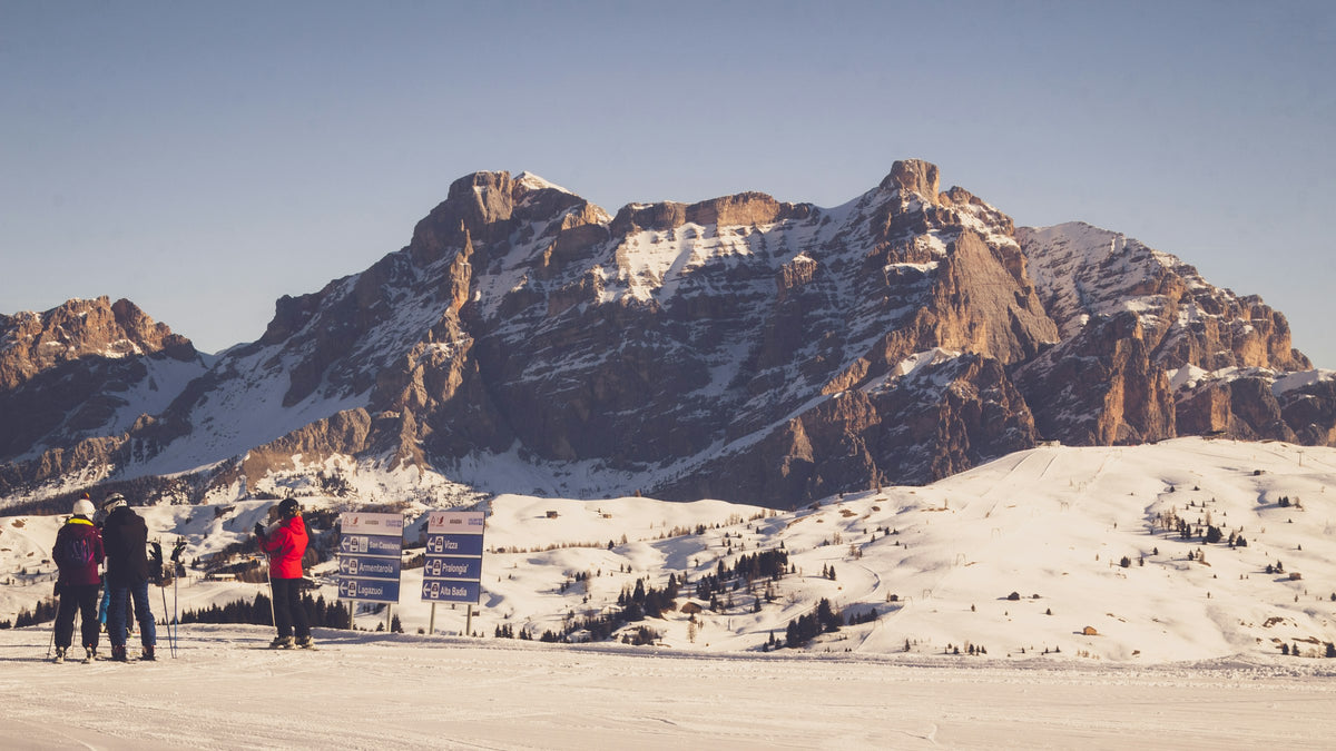 Sciatori davanti ai cartelli delle piste in Alta Badia, con il Sasso della Croce innevato