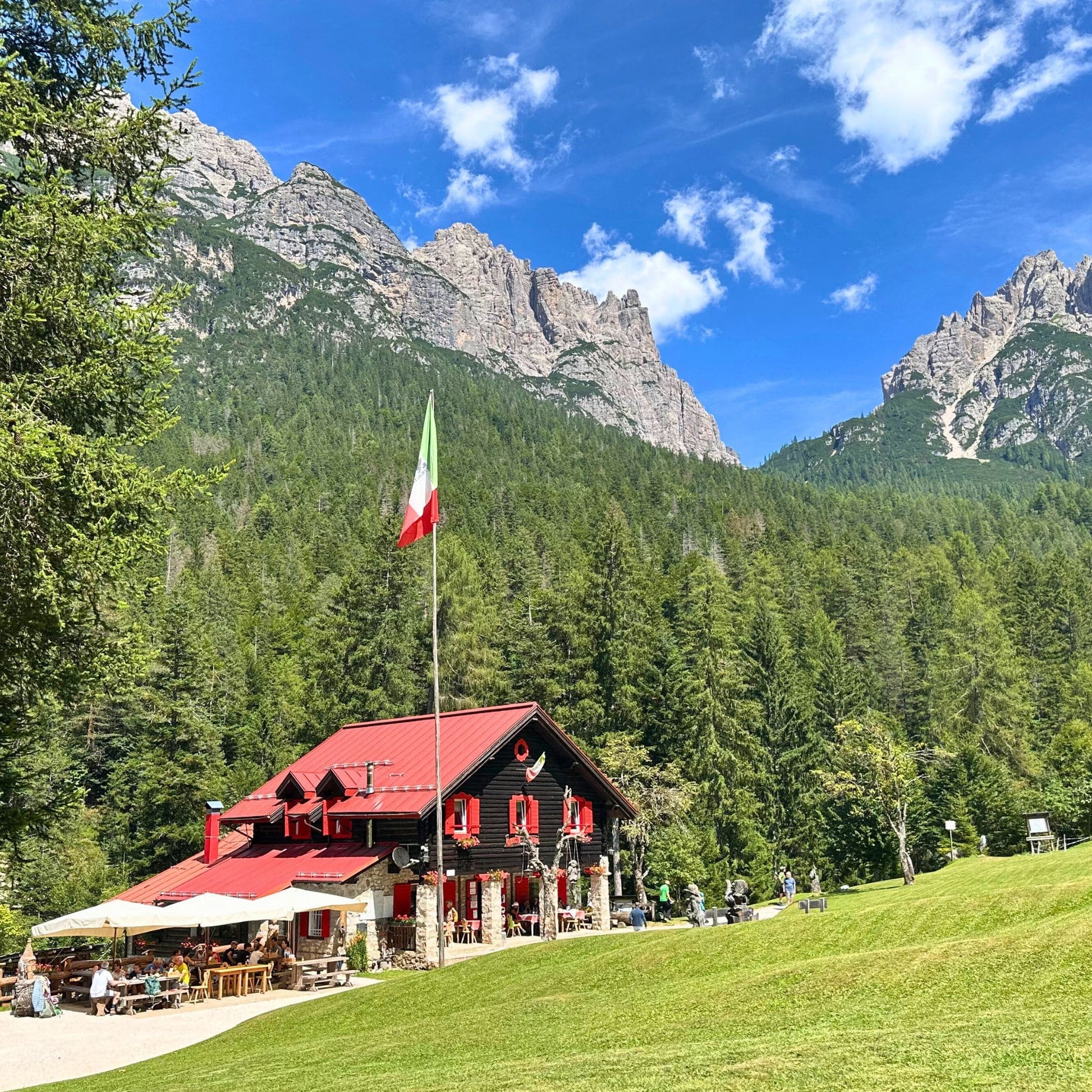 Traditional mountain rifugio with Italian flag and outdoor terrace beneath limestone peaks in Friulian Dolomites Natural Park